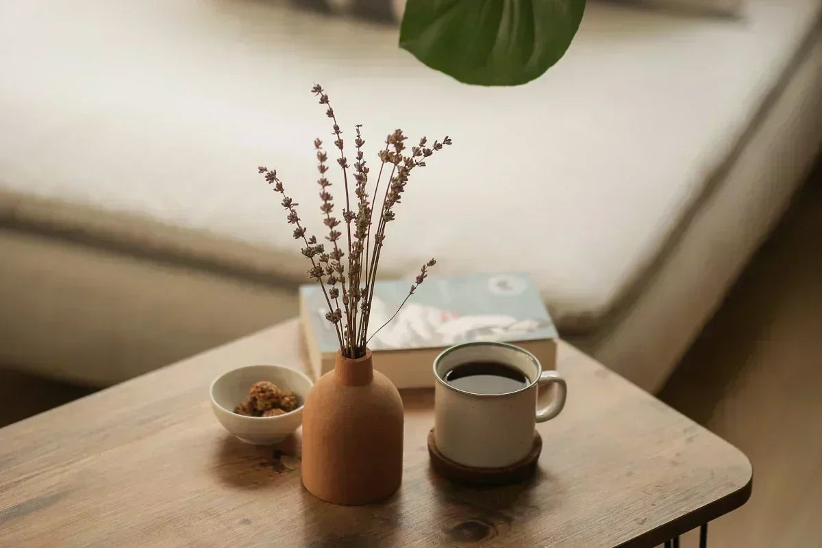 Terracotta vase with dried flowers on a wooden coffee table in a sunlit living room.