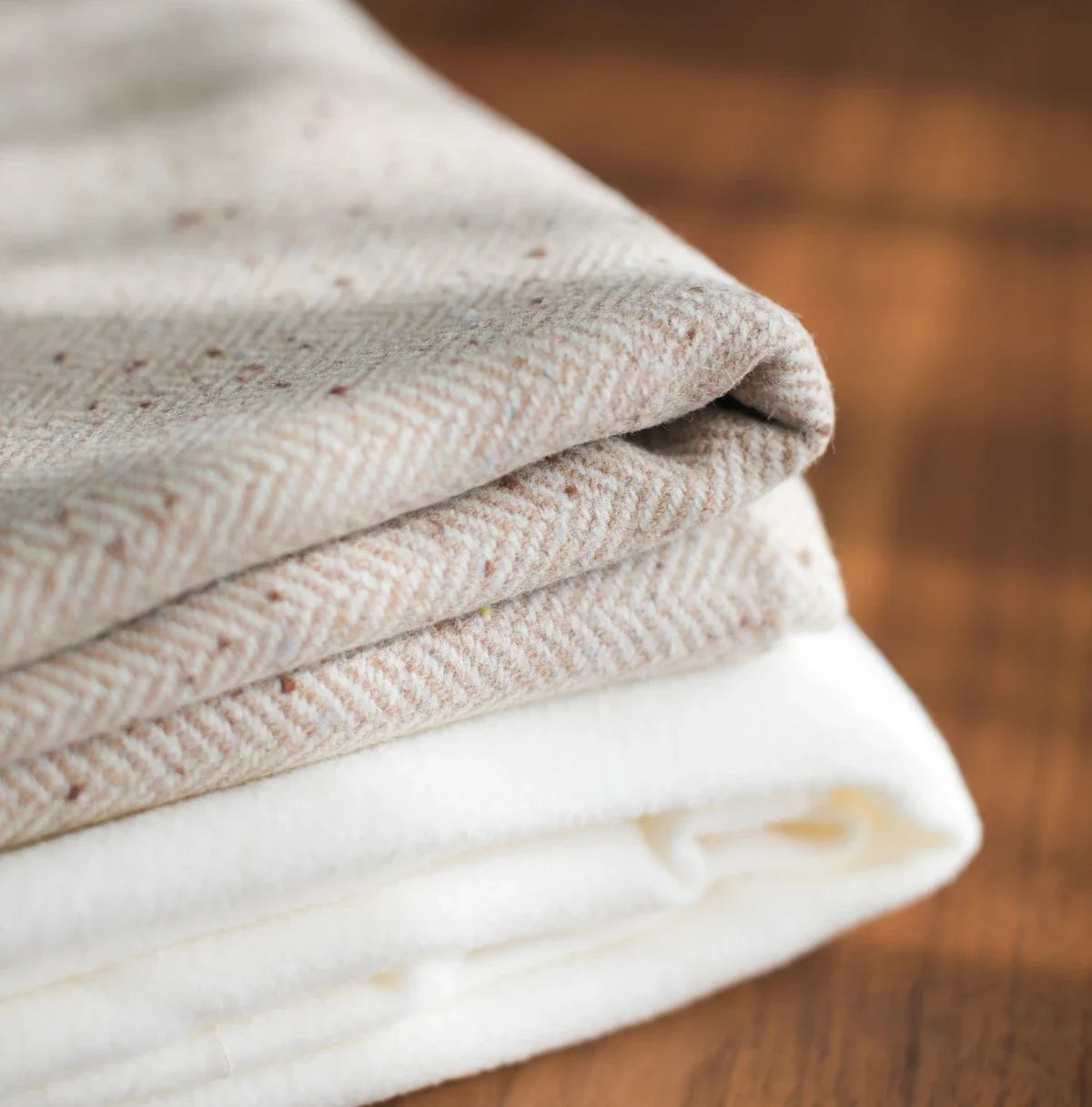 2 folded soft woollen blankets on a wooden floor.