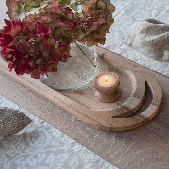 Handcrafted acacia wooden tea light holder styled with natural home accessories on a white patterned tablecloth.