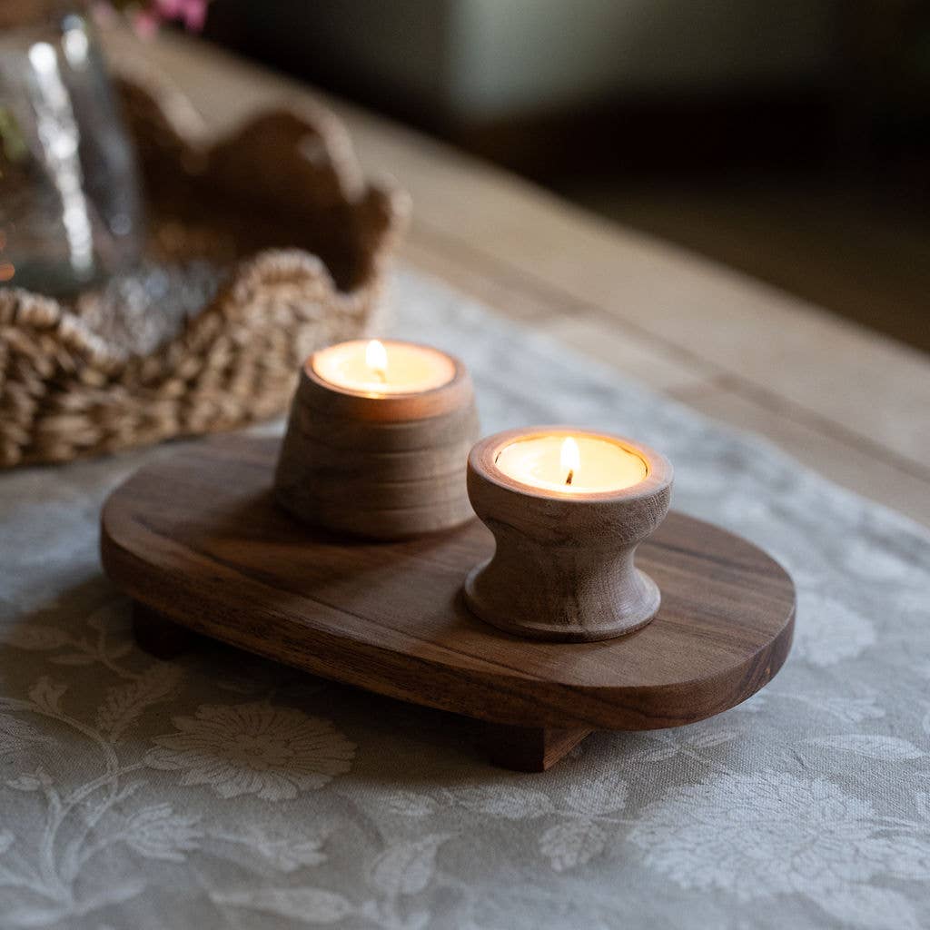 Two handcrafted wooden tea light holders glowing on an oval tray, styled with natural home accessories.