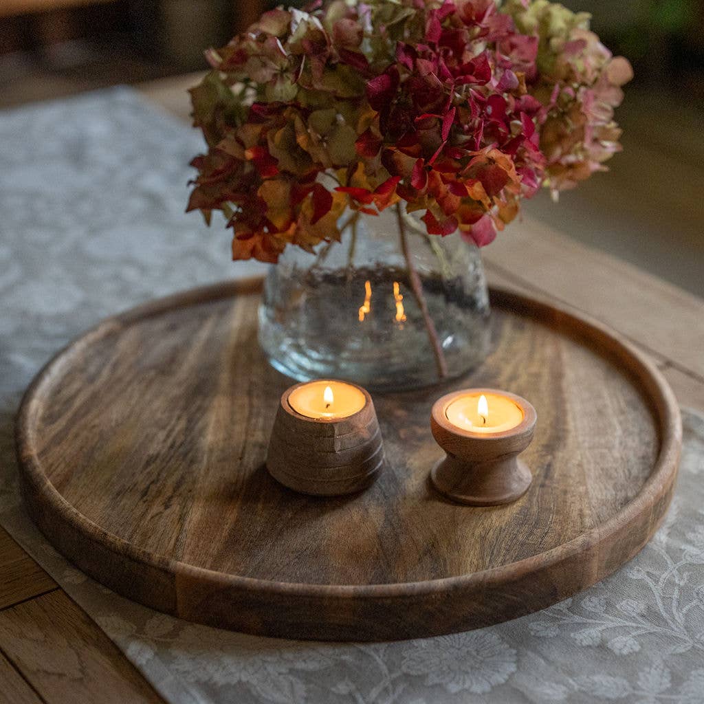 Two flickering candles in acacia wooden candle holders creating a warm indoor ambiance.