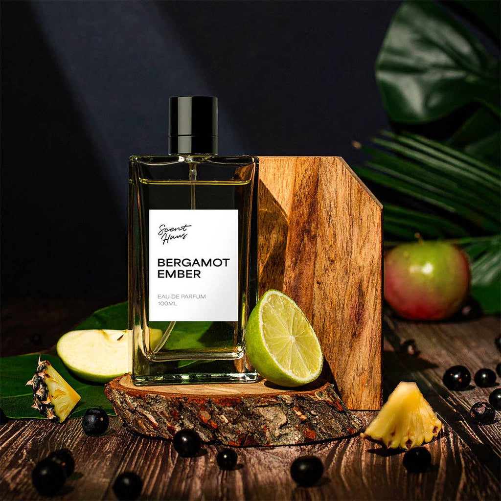 Bergamot Ember perfume bottle on a wooden stand with fruits and leaves in the background