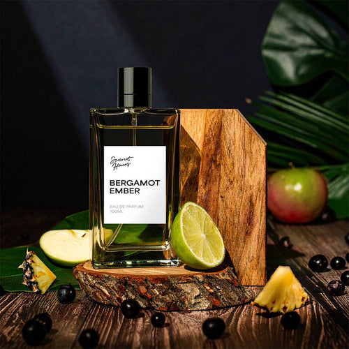 Bergamot Ember perfume bottle on a wooden stand with fruits and leaves in the background