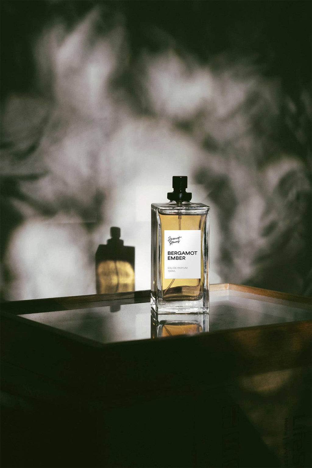 A bottle of Bergamot Amber perfume on a reflective surface with a blurred background