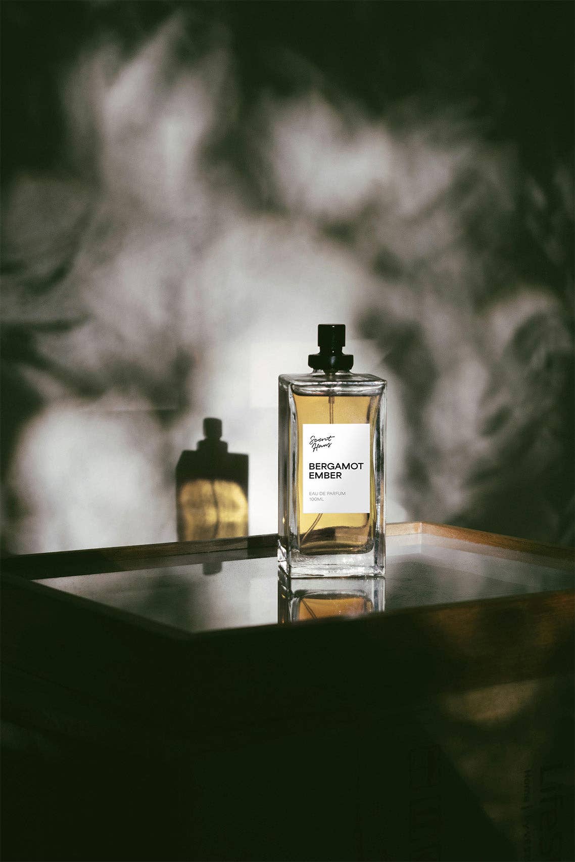 A bottle of Bergamot Amber perfume on a reflective surface with a blurred background