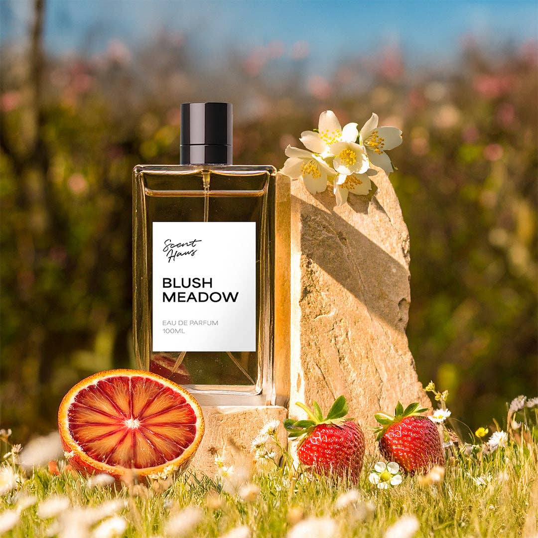Perfume bottle labeled 'Blush Meadow' with natural elements like flowers and fruit in a field setting.