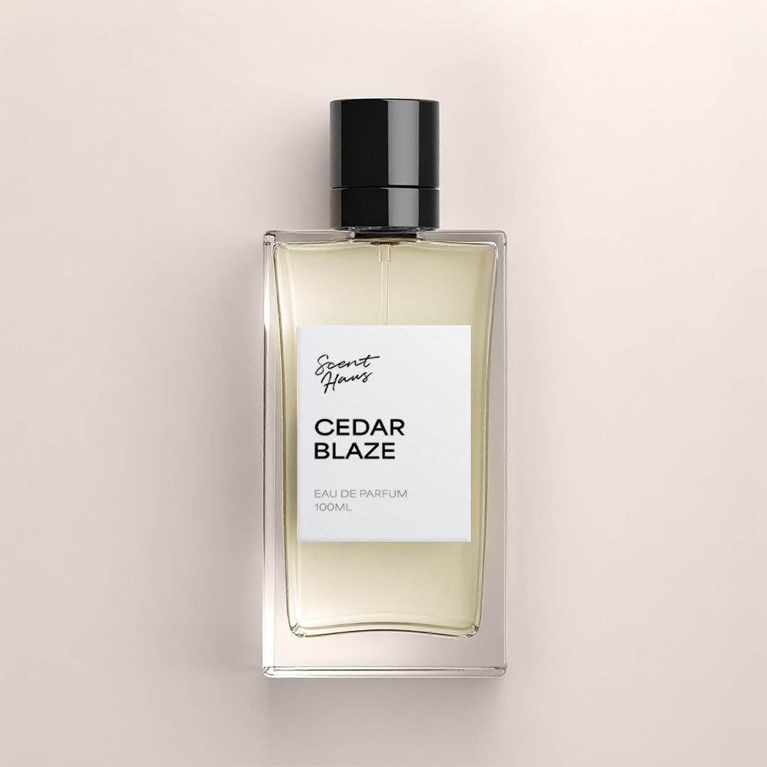 A 100ml bottle of Cedar Blaze Eau de Parfum by Scent Haus, featuring a clear glass bottle with pale yellow liquid, a white label, and a black cap, centered on a light beige background.