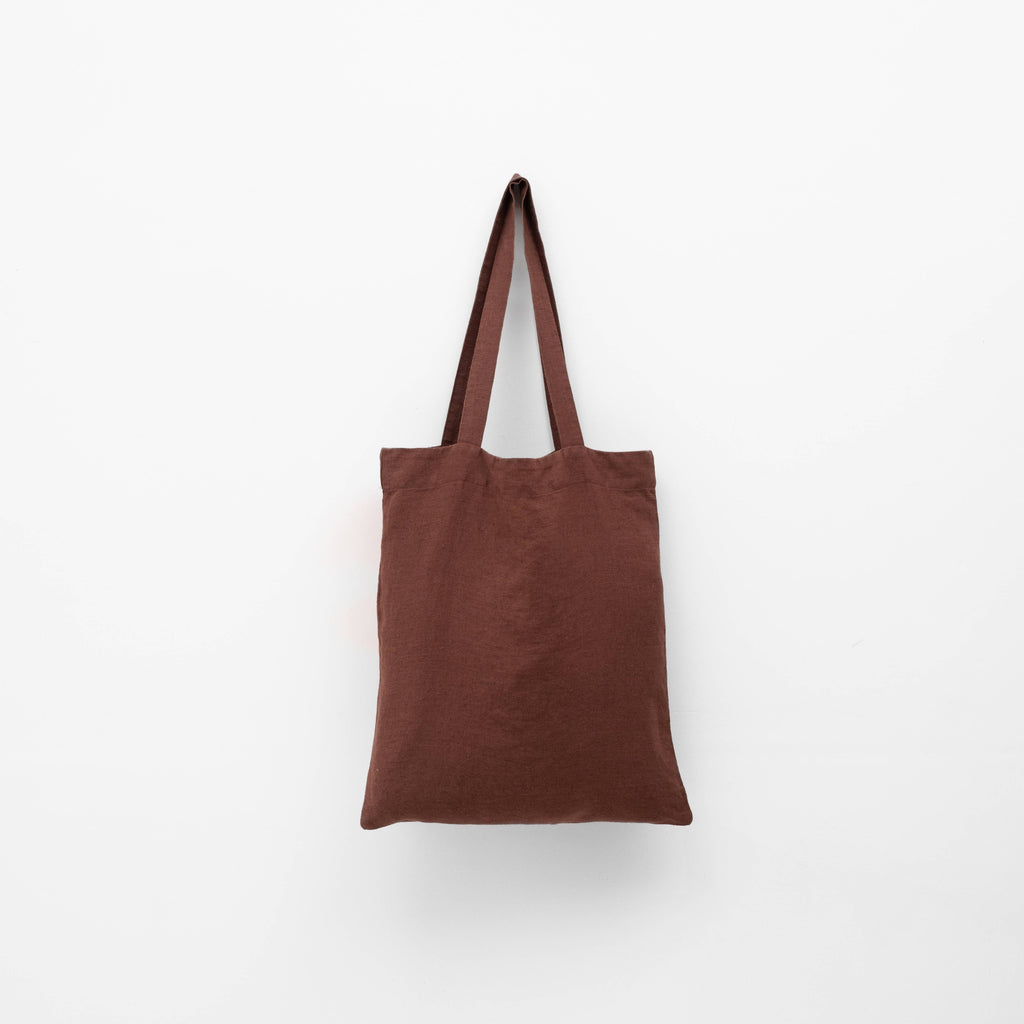 A dark brown linen tote bag with matching shoulder straps hanging against a plain white background.