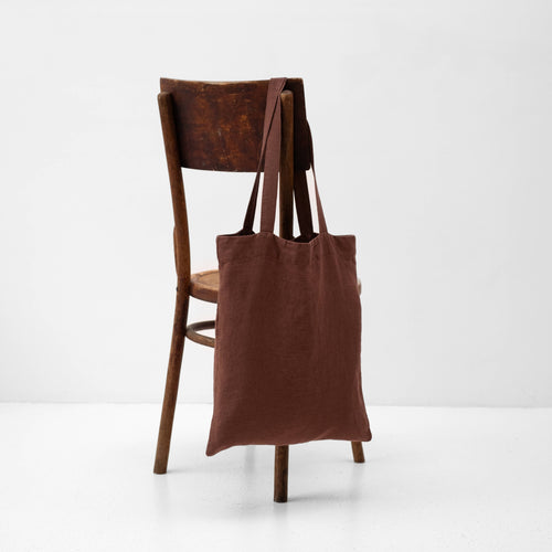 A chocolate brown linen tote bag hanging over the back of a wooden chair.