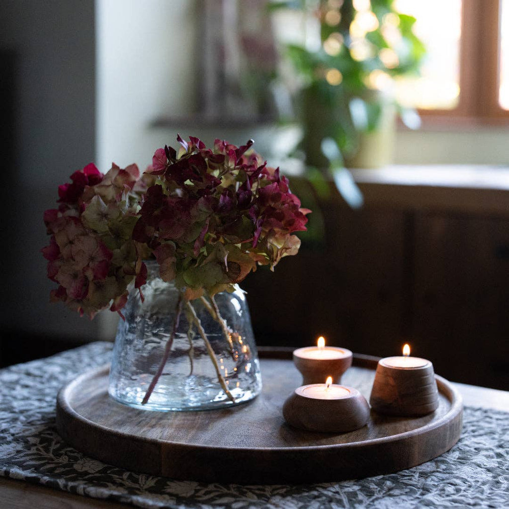 Bouquet of dried flowers in a clear vase with three candles on a Cluny round wooden tray.