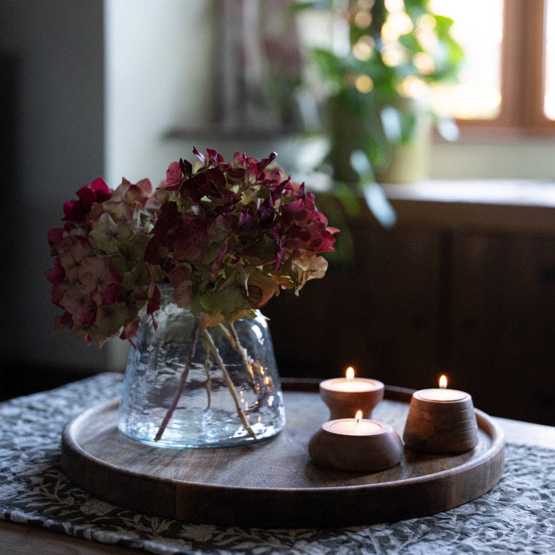 Bouquet of dried flowers in a clear vase with three candles on a Cluny round wooden tray.