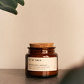 Damson plum and patchouli candle in amber glass with cork lid on a dark table.