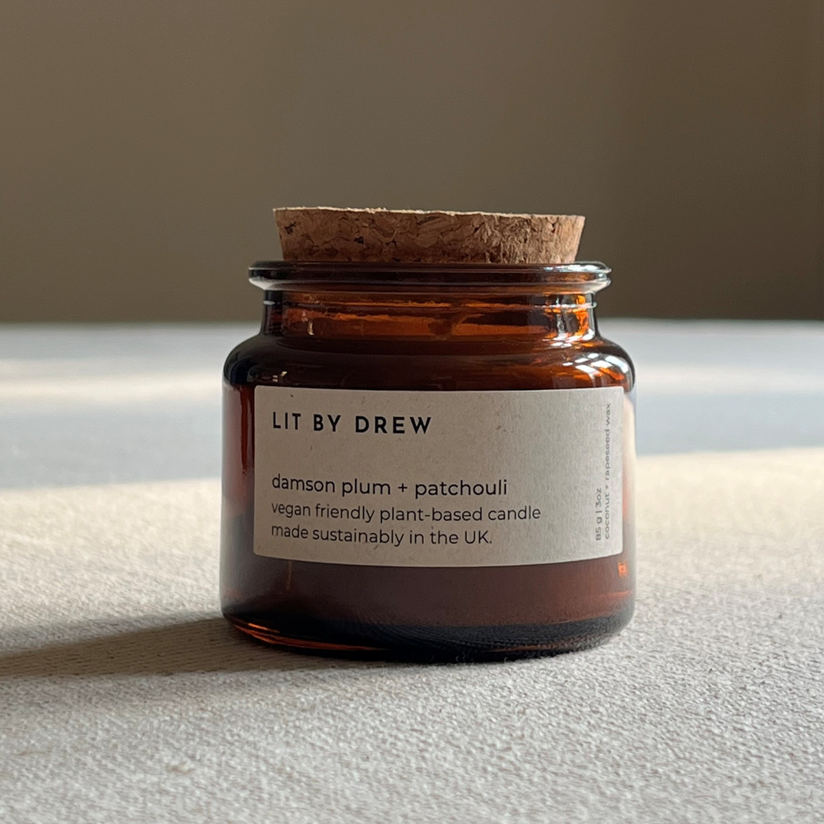 Damson plum and patchouli candle with natural cork lid styled on a bright tabletop surface.