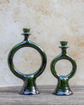Two dark green glazed handmade Moroccan ceramic ring-shaped candle holders, displayed on a rustic wooden surface against a textured beige stone wall.