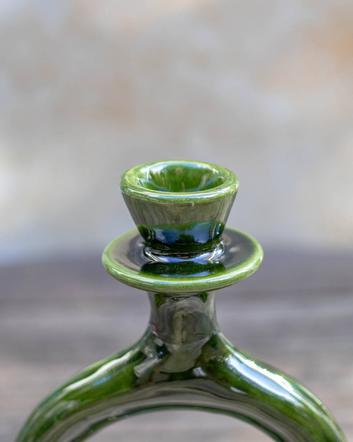 Close-up of a glossy green ceramic candle holder, photographed against a softly blurred neutral background.