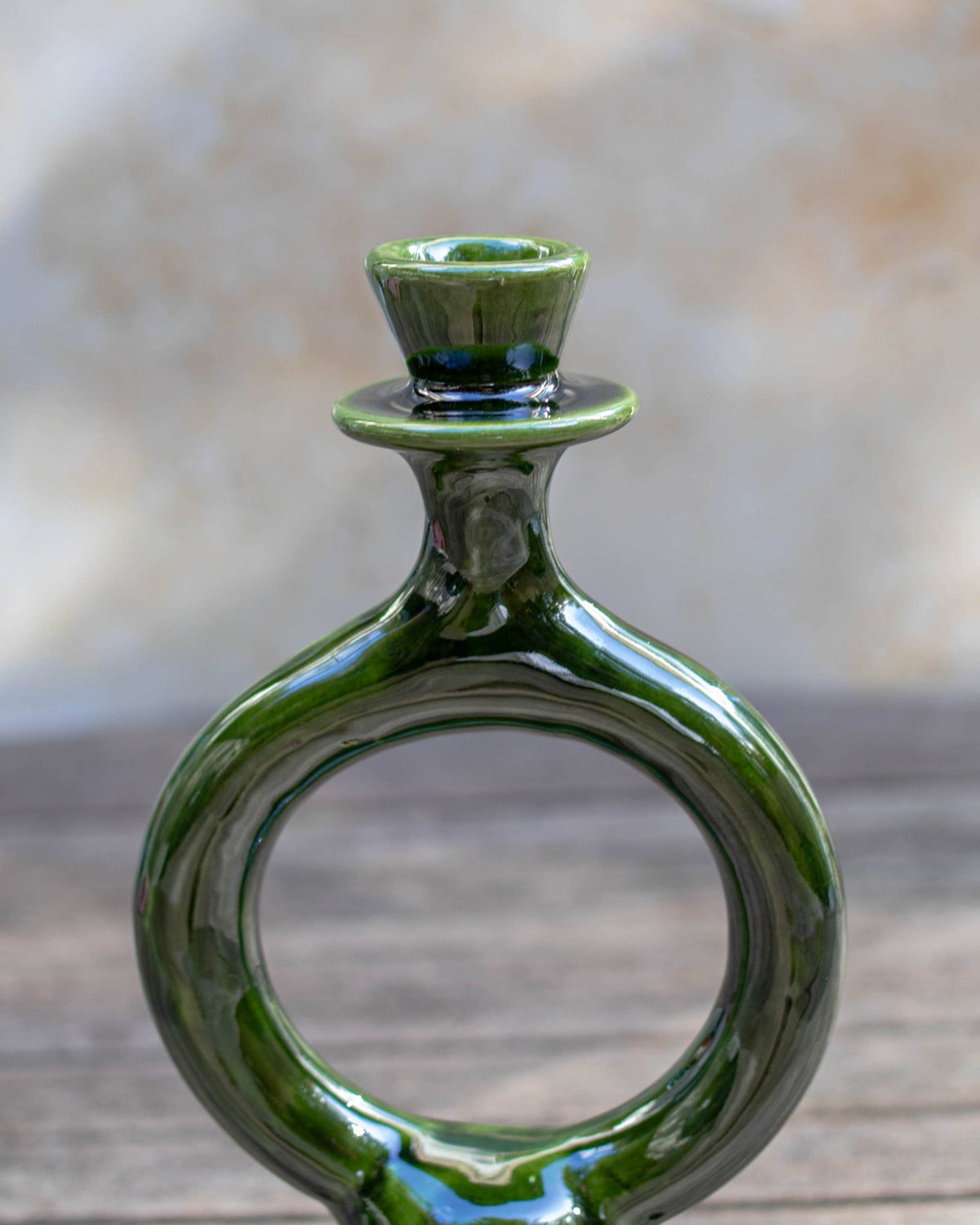 A glossy dark green handmade Moroccan ceramic candle holder with a unique circular ring body, set against a blurred rustic background.
