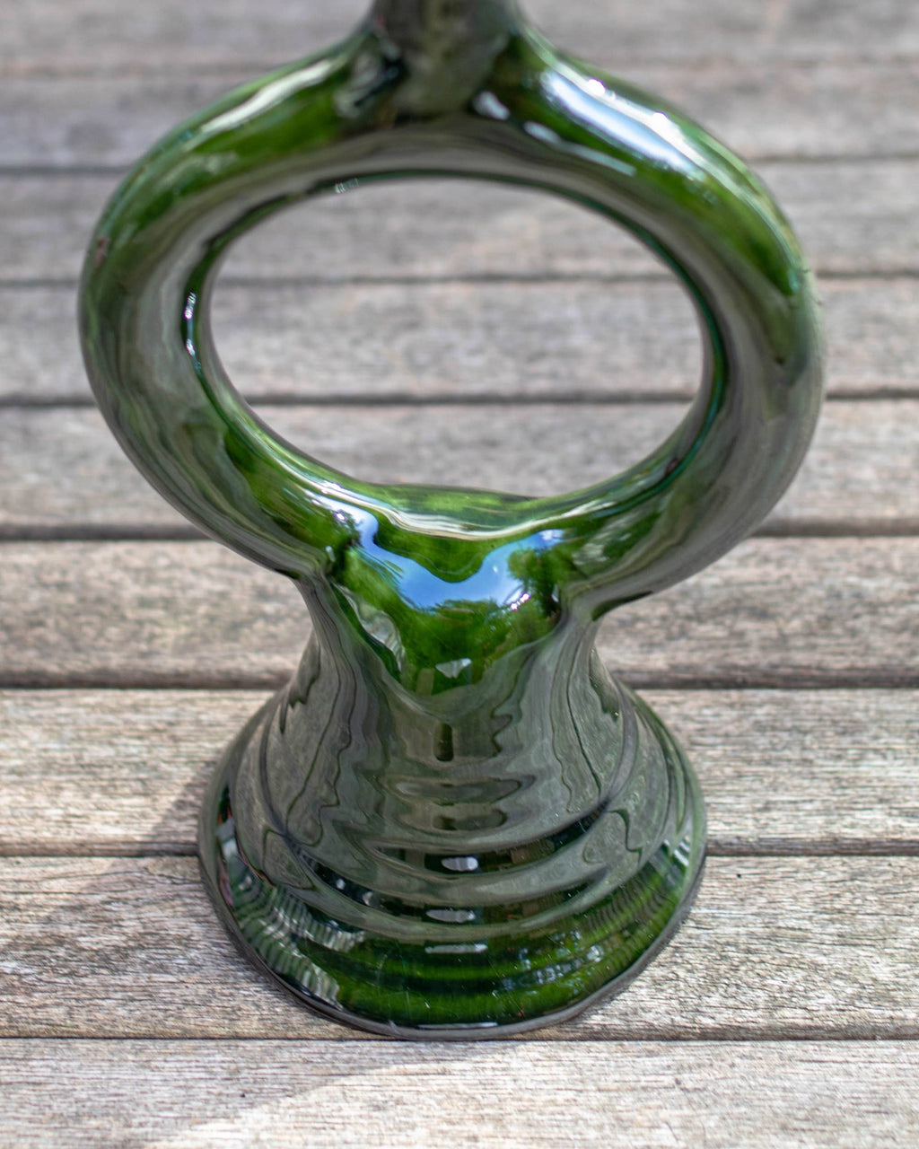 A glossy dark green ceramic candle holder with a wide ring opening and a flared base, photographed on a weathered wooden surface.