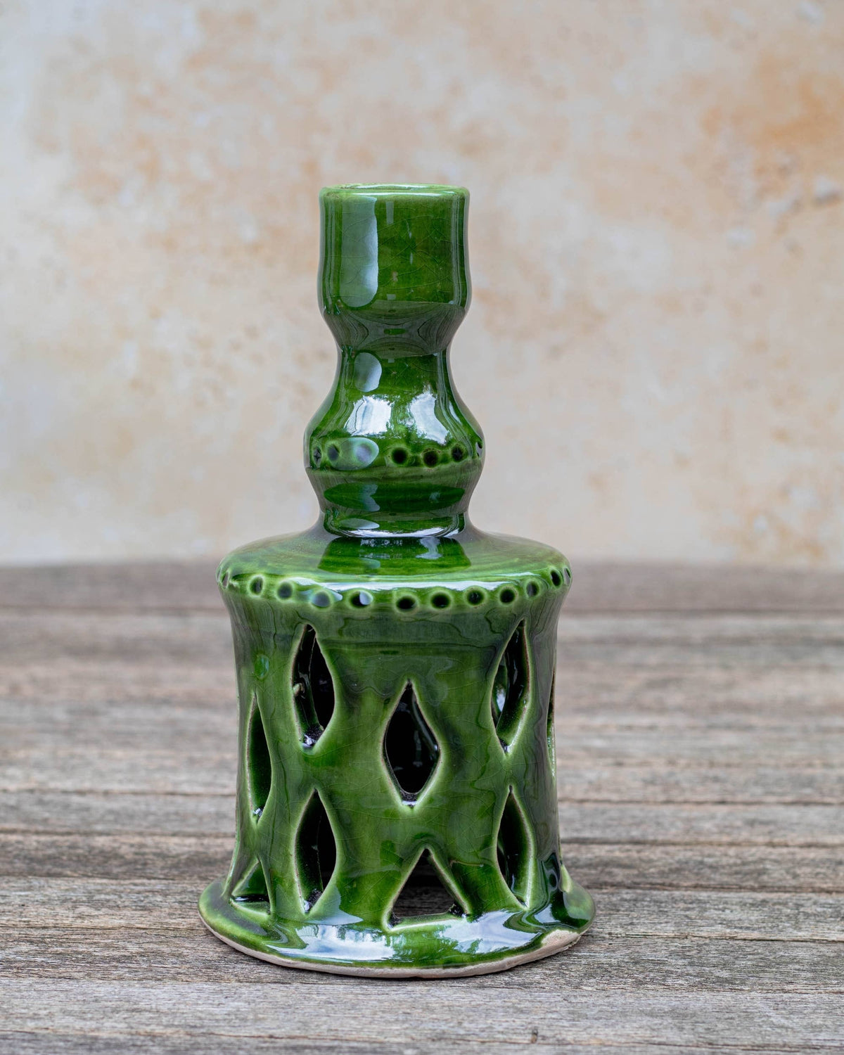 Green ceramic candle holder on a wooden surface with a beige background