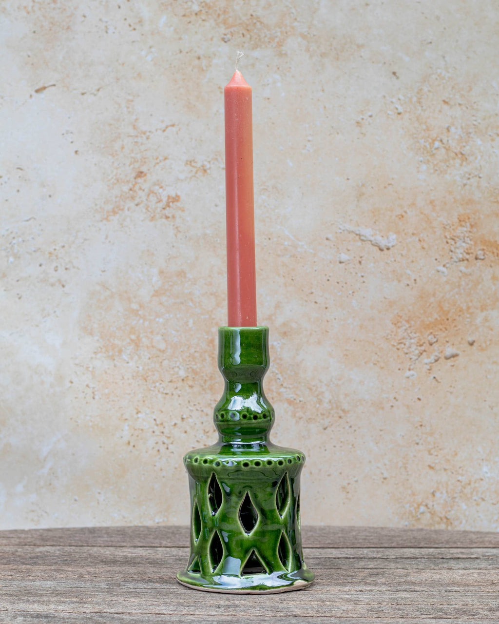 Green ceramic candle holder with a pink candle on a textured surface