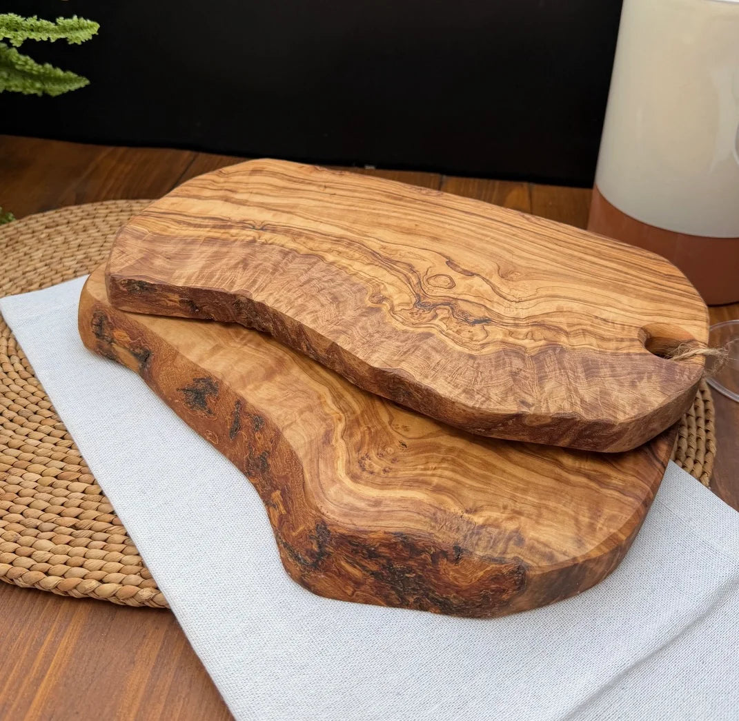 Two irregular edged olive wood serving boards stacked on a white cloth over a woven placemat.