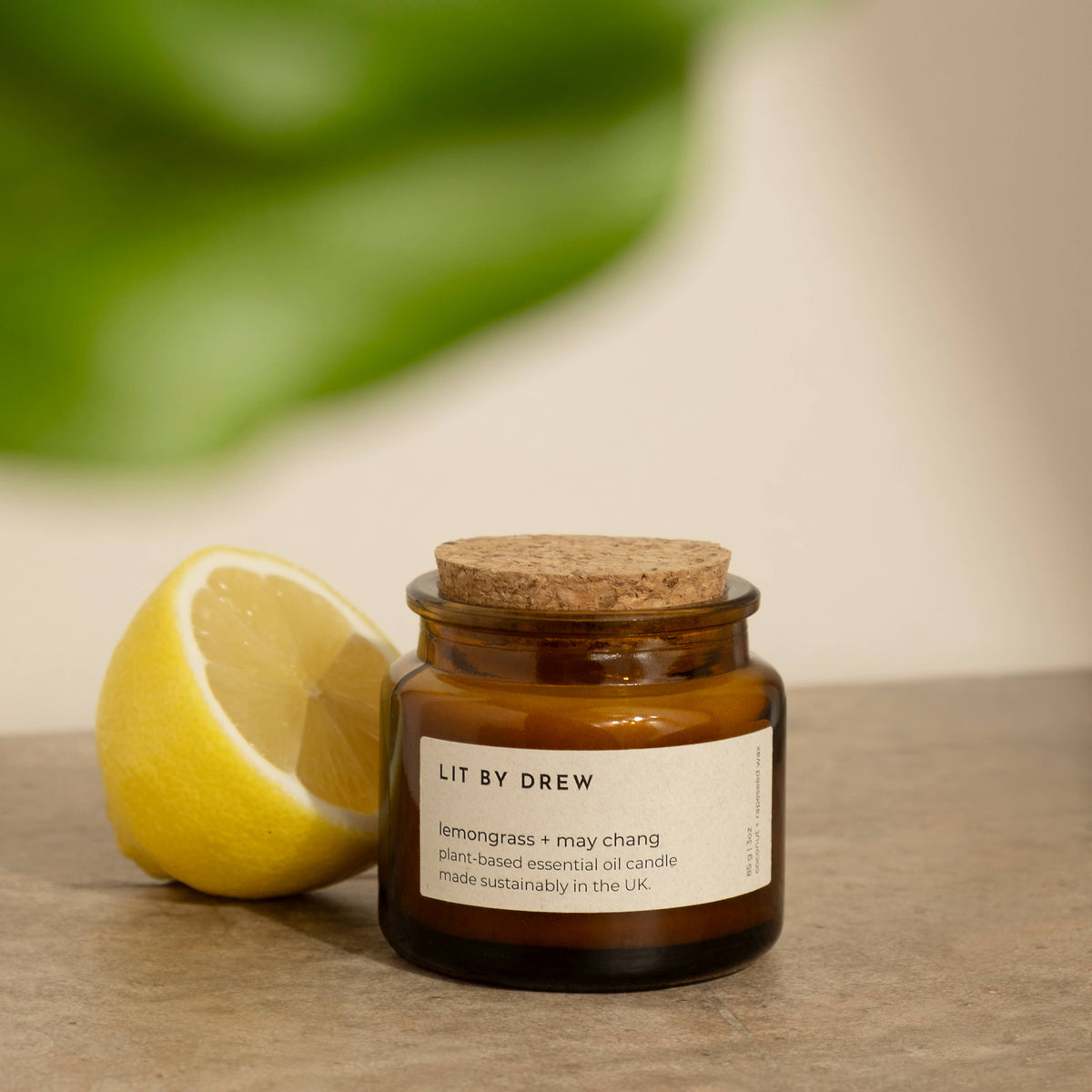 Lemongrass essential oil candle in amber glass with cork lid styled beside a fresh lemon.