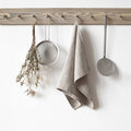A wooden pegboard hanging on a plain white wall, styled with kitchen utensils and a natural linen towel.