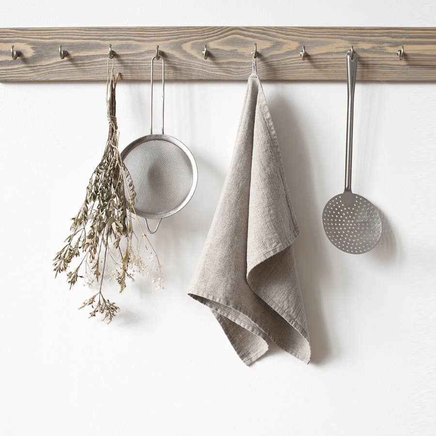 A wooden pegboard hanging on a plain white wall, styled with kitchen utensils and a natural linen towel.