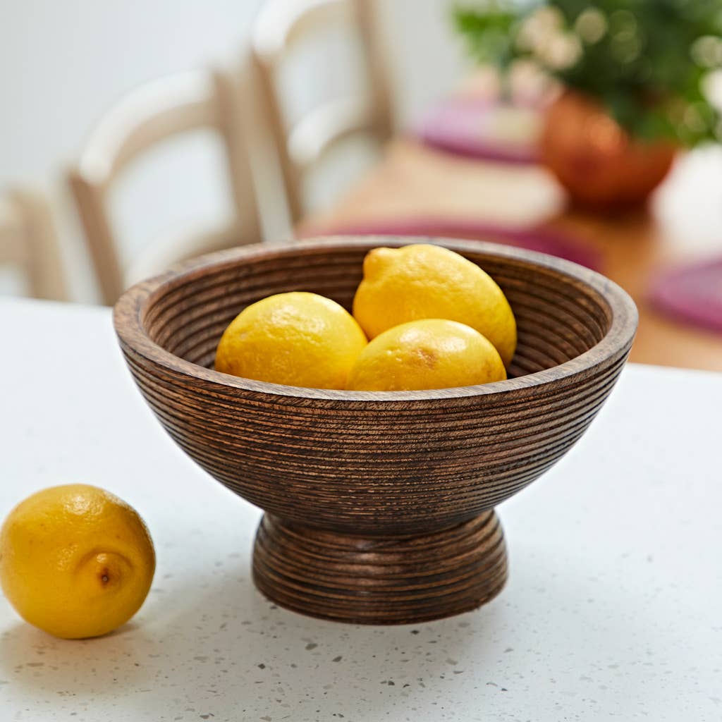 Mango wood pedestal bowl with ribbed texture filled with lemons on a table.