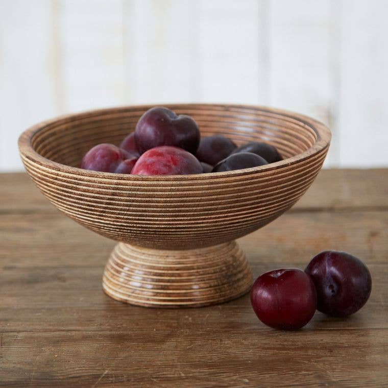 Natural mango wood bowl filled with plums displayed on a smooth wooden surface.