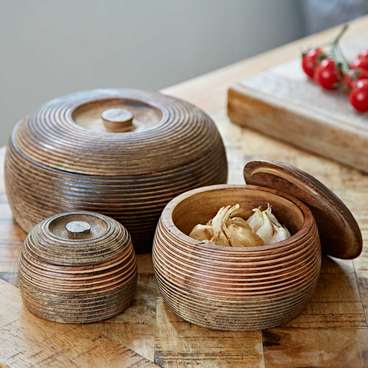Natural mango wood storage bowls with wooden lids displayed on a matching wooden table.