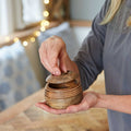 Close-up of hands holding a small natural mango wood storage bowl with a soft blurred background.