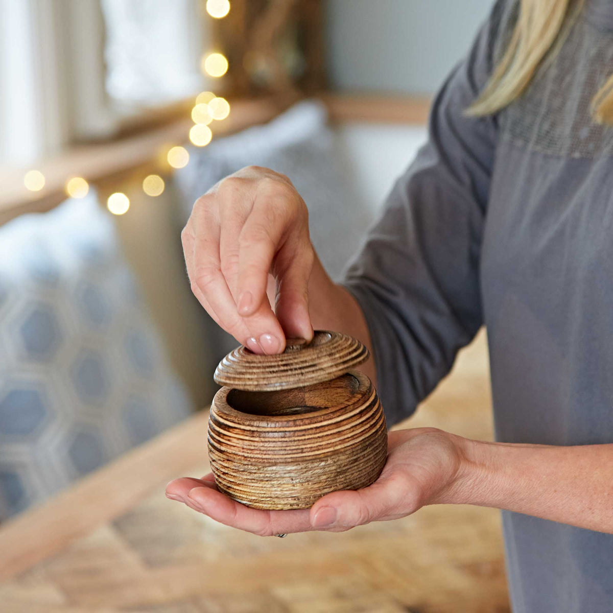 Close-up of hands holding a small natural mango wood storage bowl with a soft blurred background.