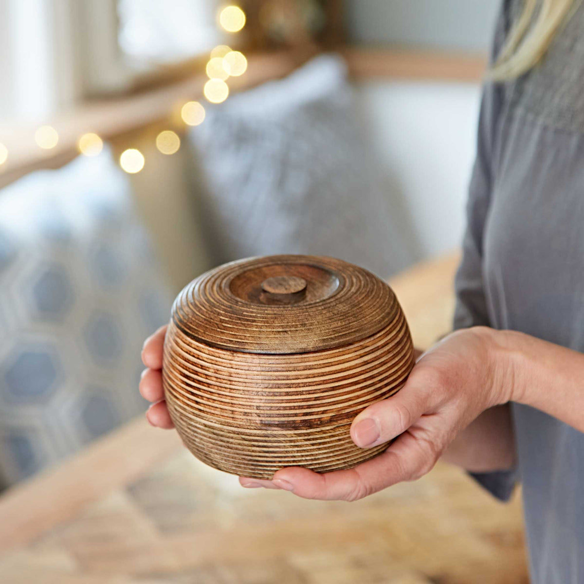 Natural mango wood bowl with lid held in hand against a warm indoor background.