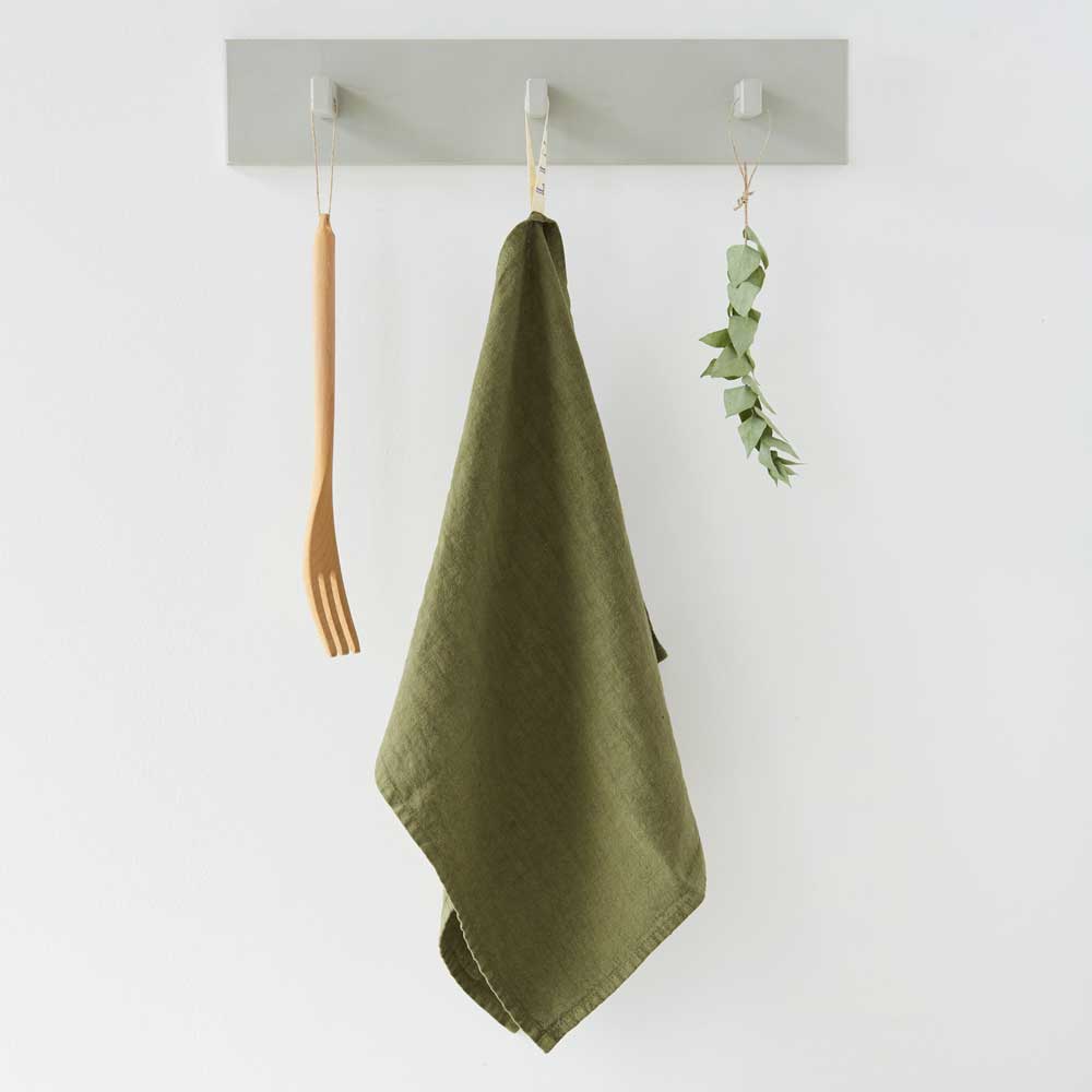 A martini olive green linen kitchen towel hanging from a wall hook against a plain white background.