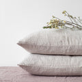 Two light gray melange linen pillowcases stacked neatly on a bed, styled with a delicate flower branch on top against a crisp white background.