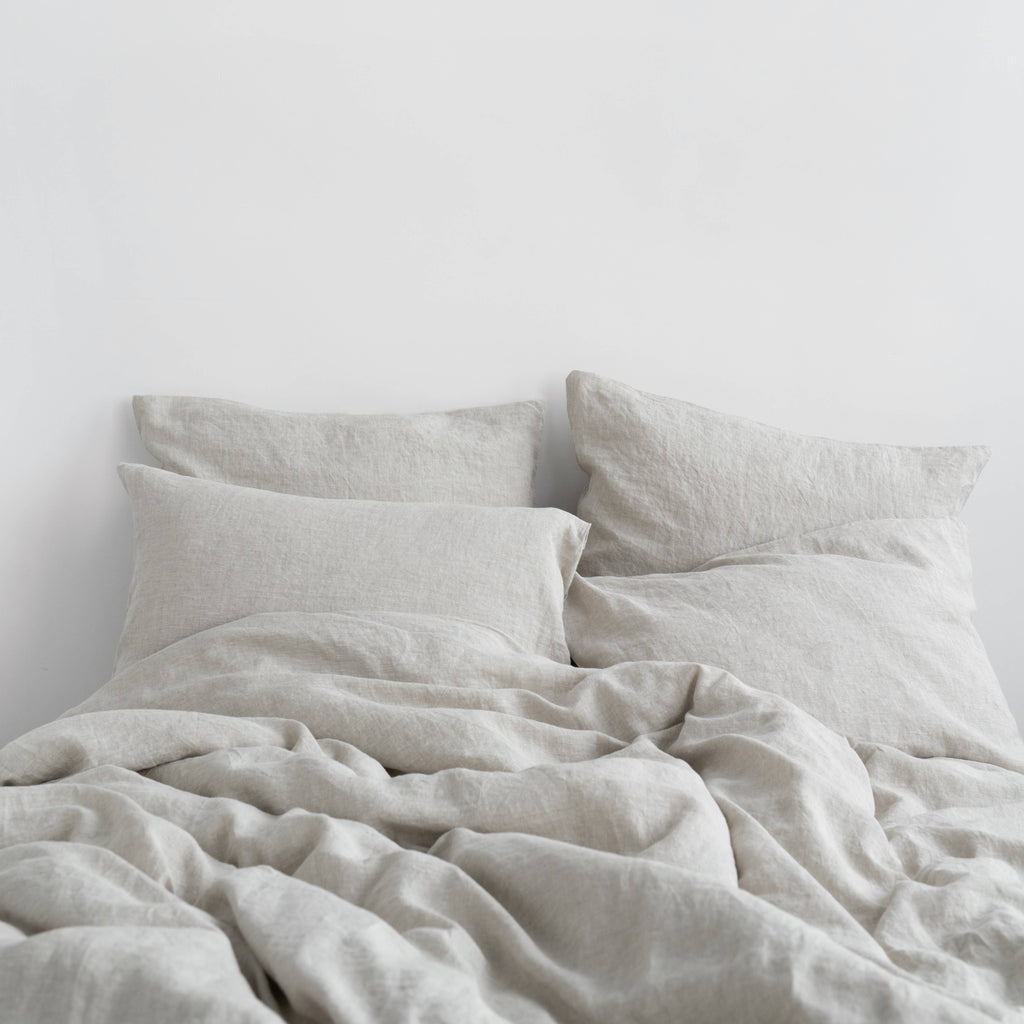 Light beige linen bedding set featuring a relaxed, rumpled duvet and two matching pillowcases on a bed against a plain white wall.