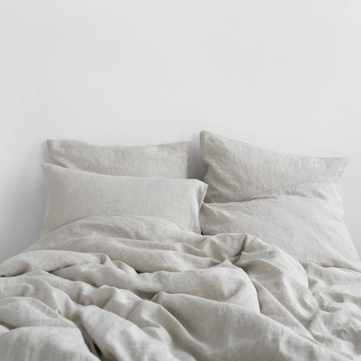 Light beige linen bedding set featuring a relaxed, rumpled duvet and two matching pillowcases on a bed against a plain white wall.
