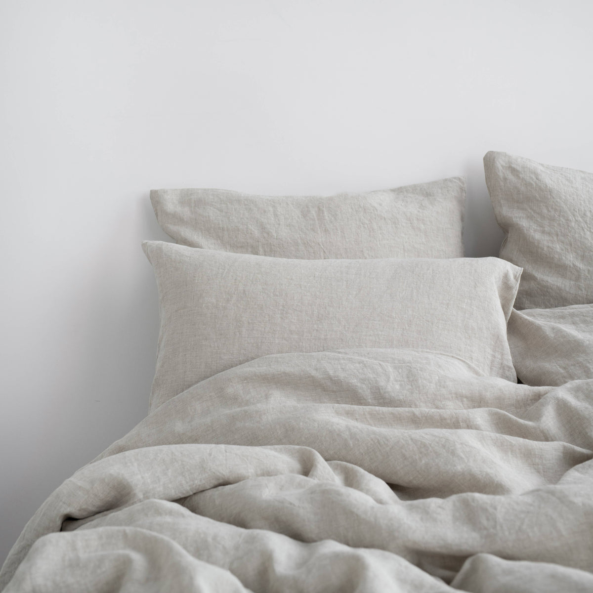 Light beige linen bedding set featuring a relaxed, rumpled duvet and two matching pillowcases on a bed against a plain white wall.