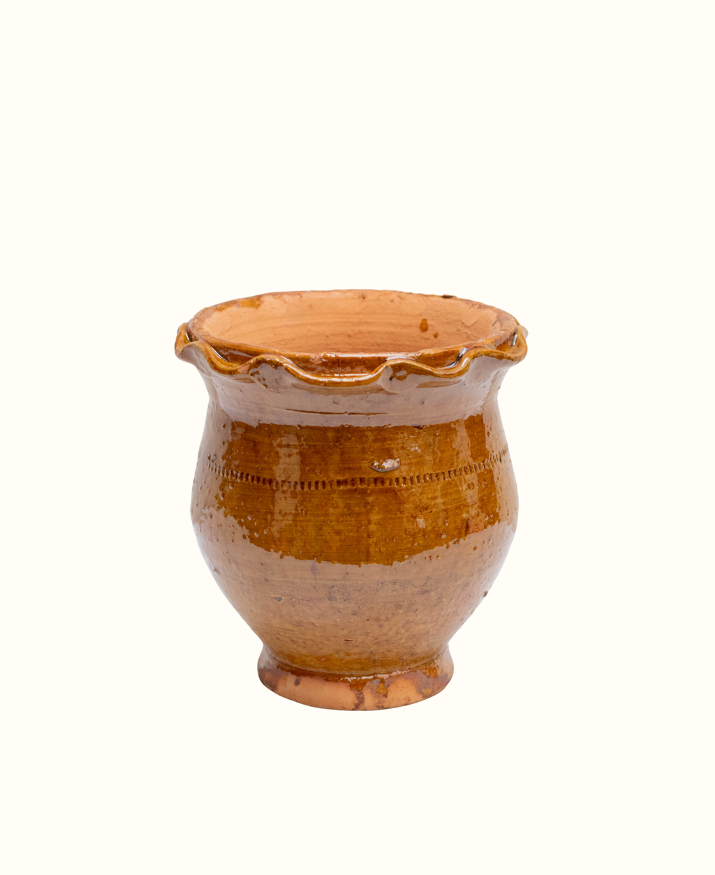 A small handmade terracotta plant pot with a scalloped rim and a footed base, glazed in a warm amber-brown color with darker brown speckles, isolated on a white background.
