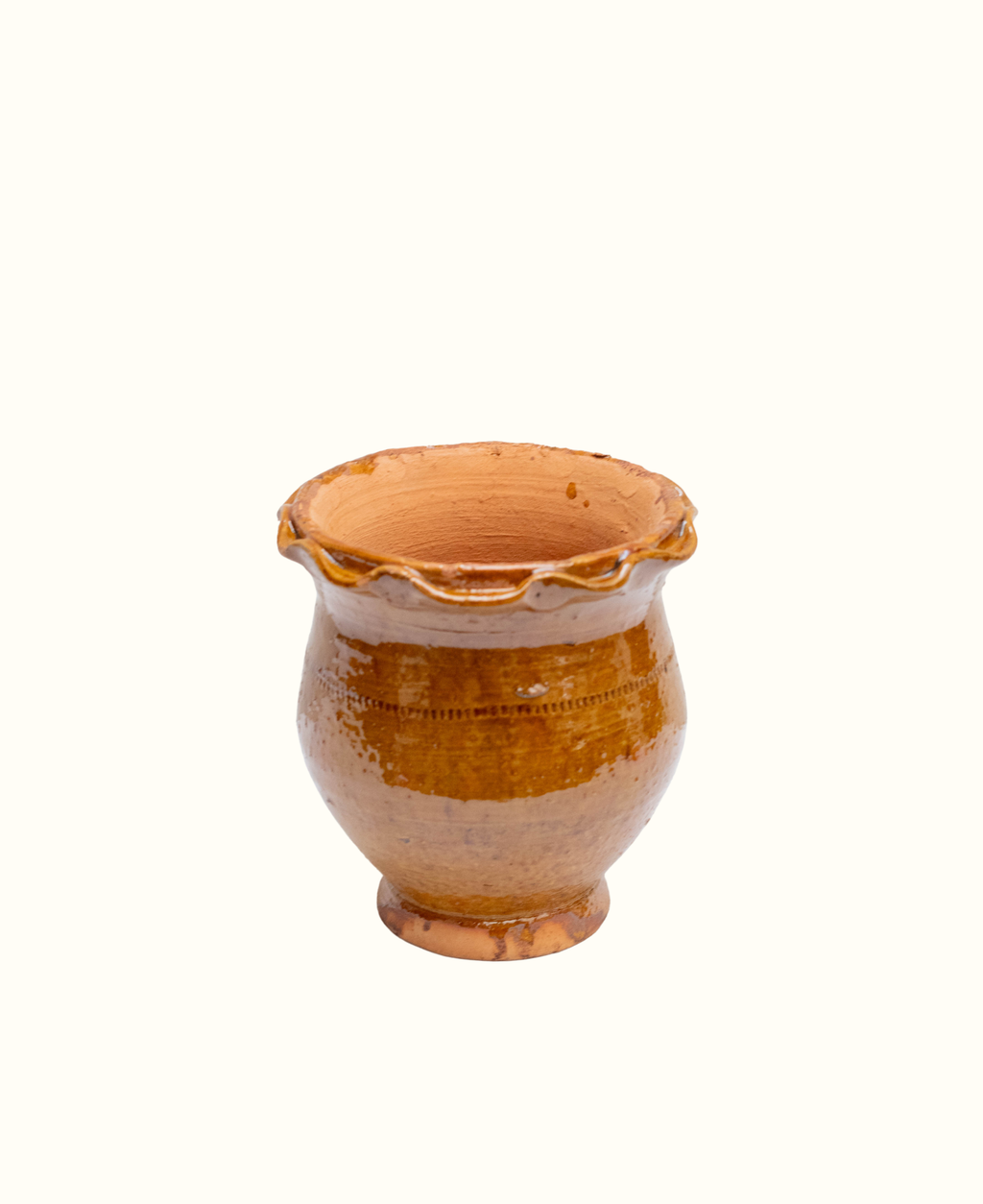 A small handmade terracotta plant pot with a scalloped rim and a rounded body, glazed in a warm amber-brown glaze on a plain white background.