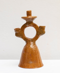 A handmade ceramic three-light candle holder with a unique ring-shaped back and a textured, glossy brown glaze, set against a plain off-white background.