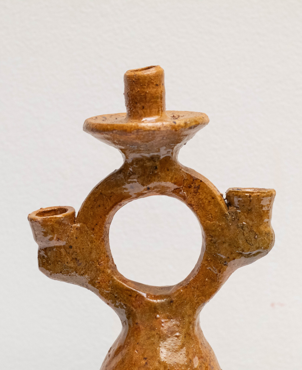 A close-up of a handmade terracotta three-light candle holder with a rustic, earthy ochre glaze, set against a plain off-white background.