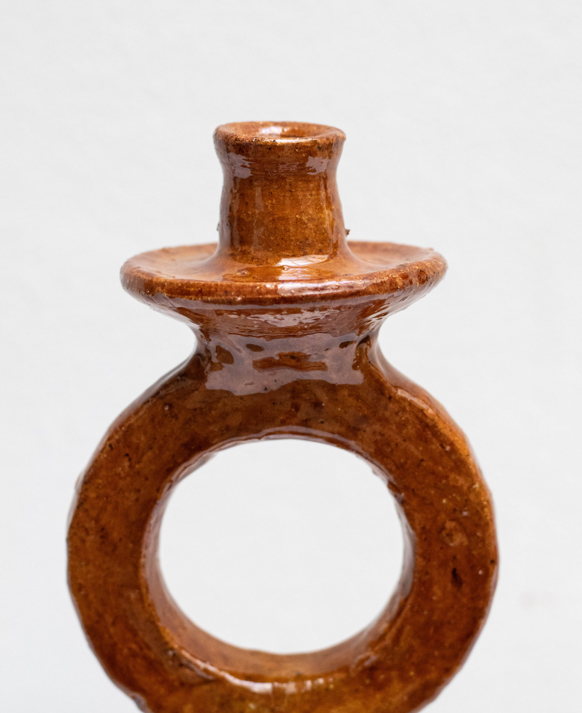 A close up of a handmade terracotta ring-shaped candle holder with a glossy brown glaze, photographed against a plain white background.