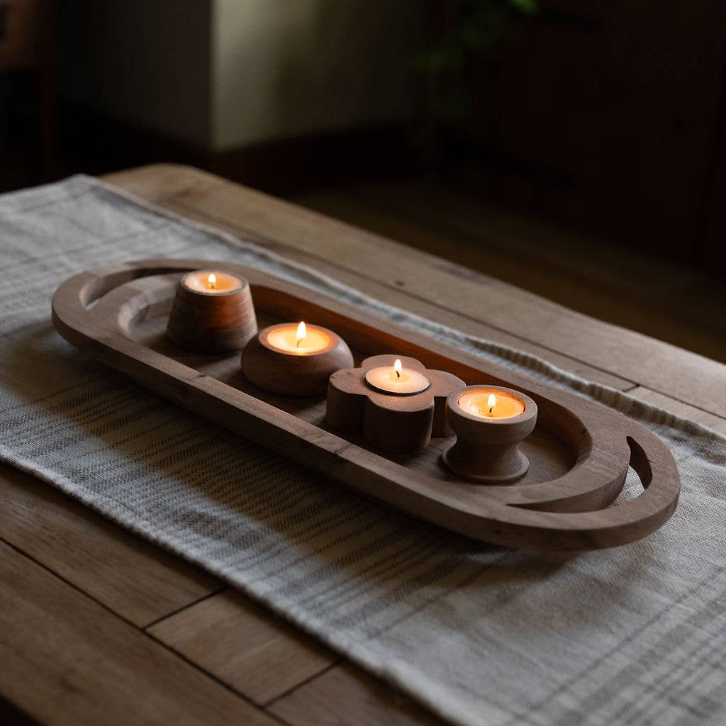 Four wooden tea light candle holders holding lit tealight candles, placed on a woven runner over a wooden table in a dimly lit interior.