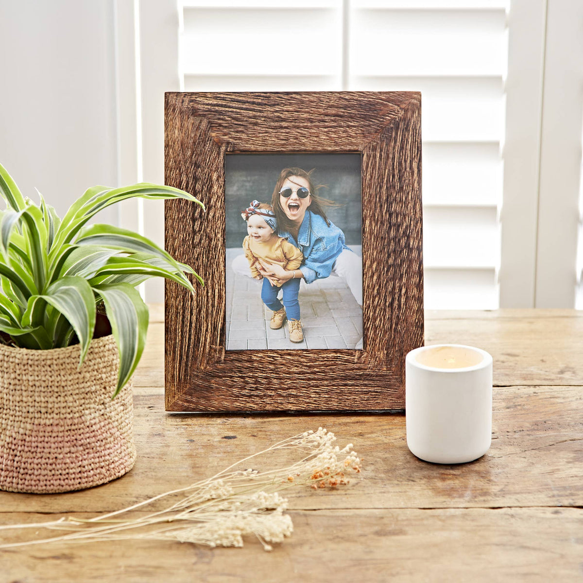 Rustic brown wooden photo frame with a family picture on a table near a plant and candle holder.