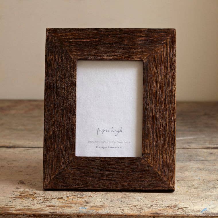 Dark brown wooden photo frame with a weathered finish on a distressed wooden table.