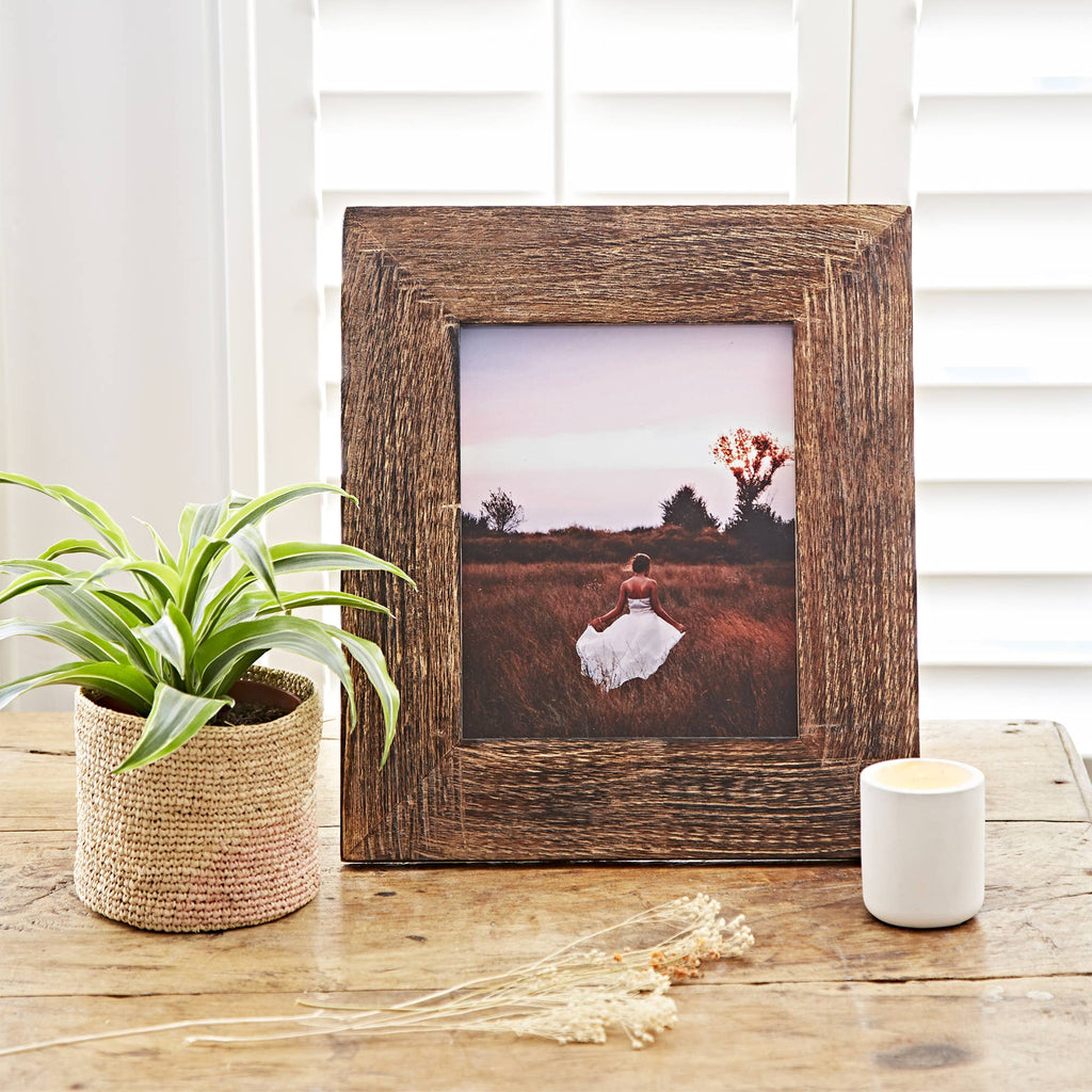 Natural wooden picture frame with a woman in a field styled on a wooden tabletop.