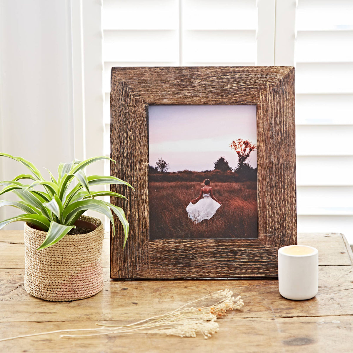 Natural wooden picture frame with a woman in a field styled on a wooden tabletop.