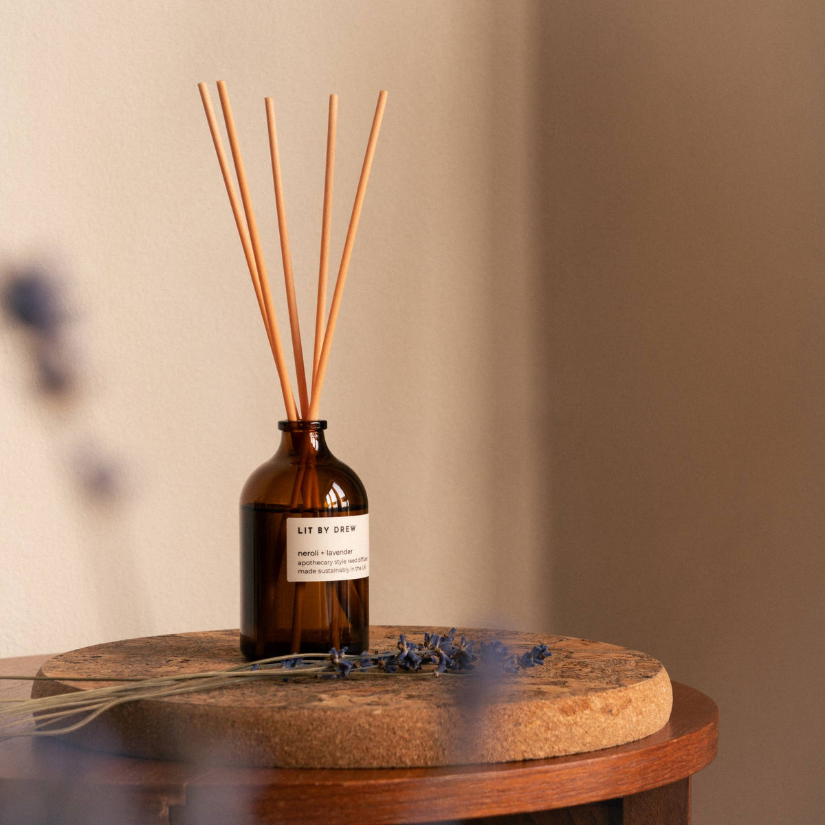 Amber glass reed diffuser bottle with natural wood reeds on a wooden table against a beige wall.