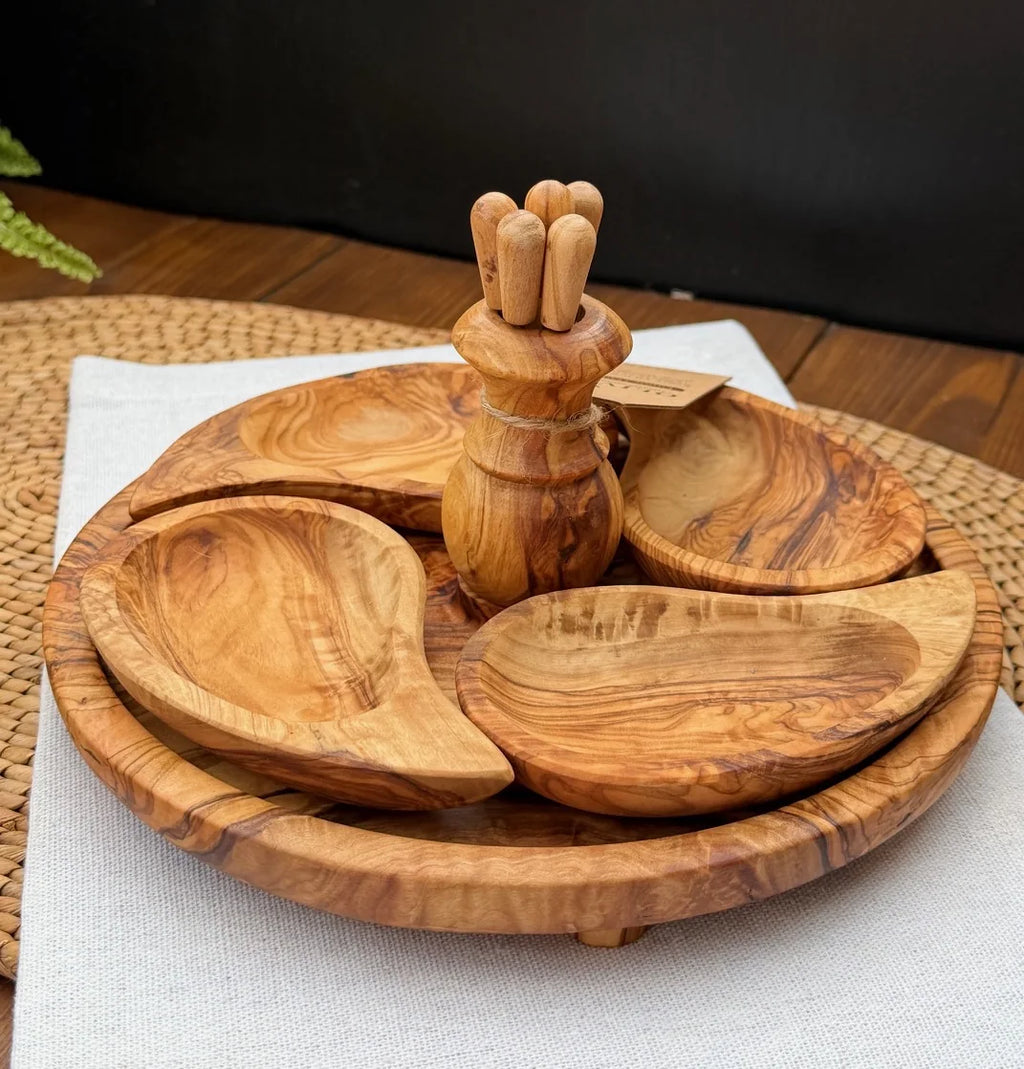 Olive wood appetiser set with serving dishes and utensil holder on a woven placemat over a white cloth.
